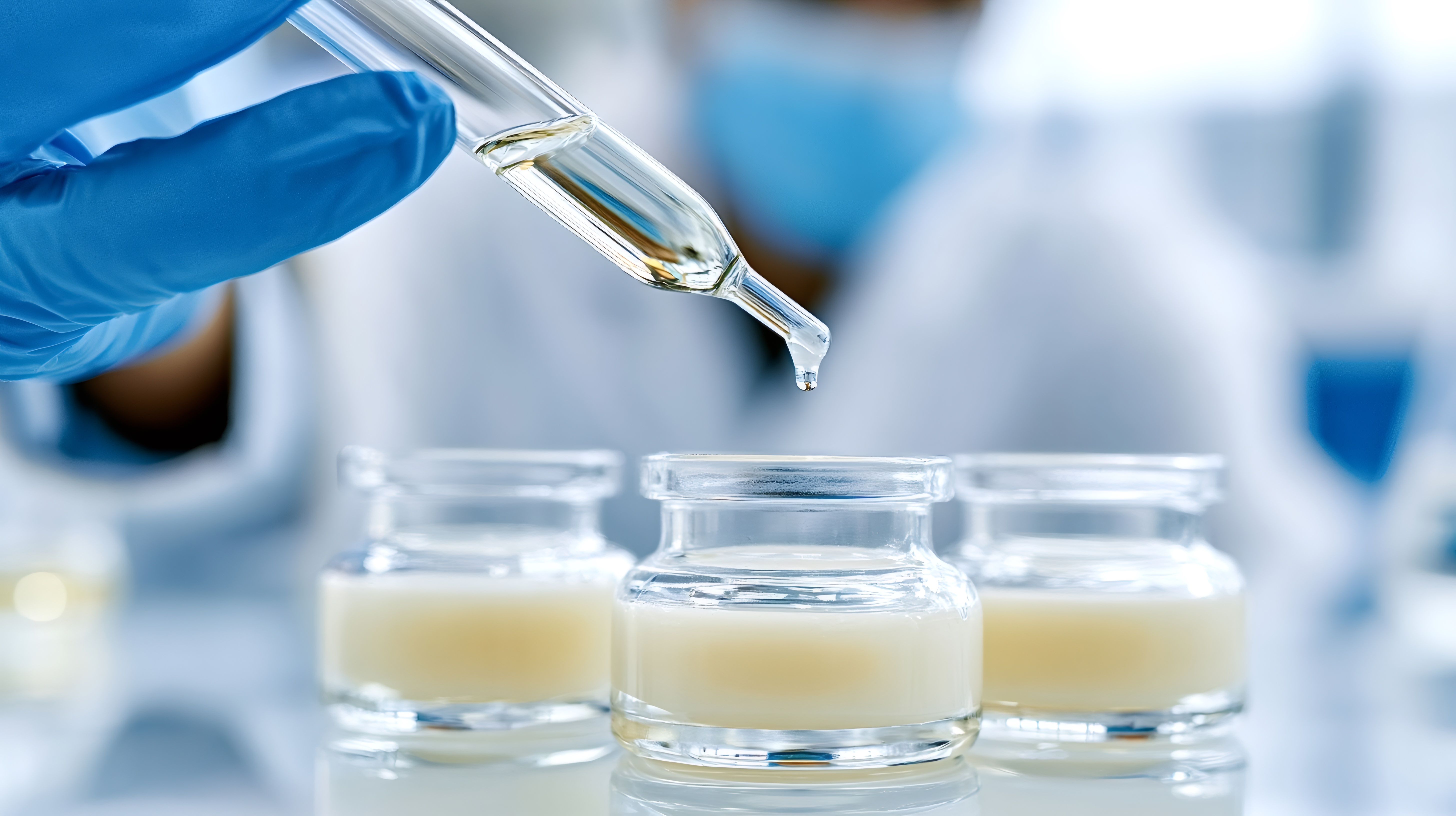Scientist in blue gloves using pipette to dispense golden liquid into laboratory glass vials