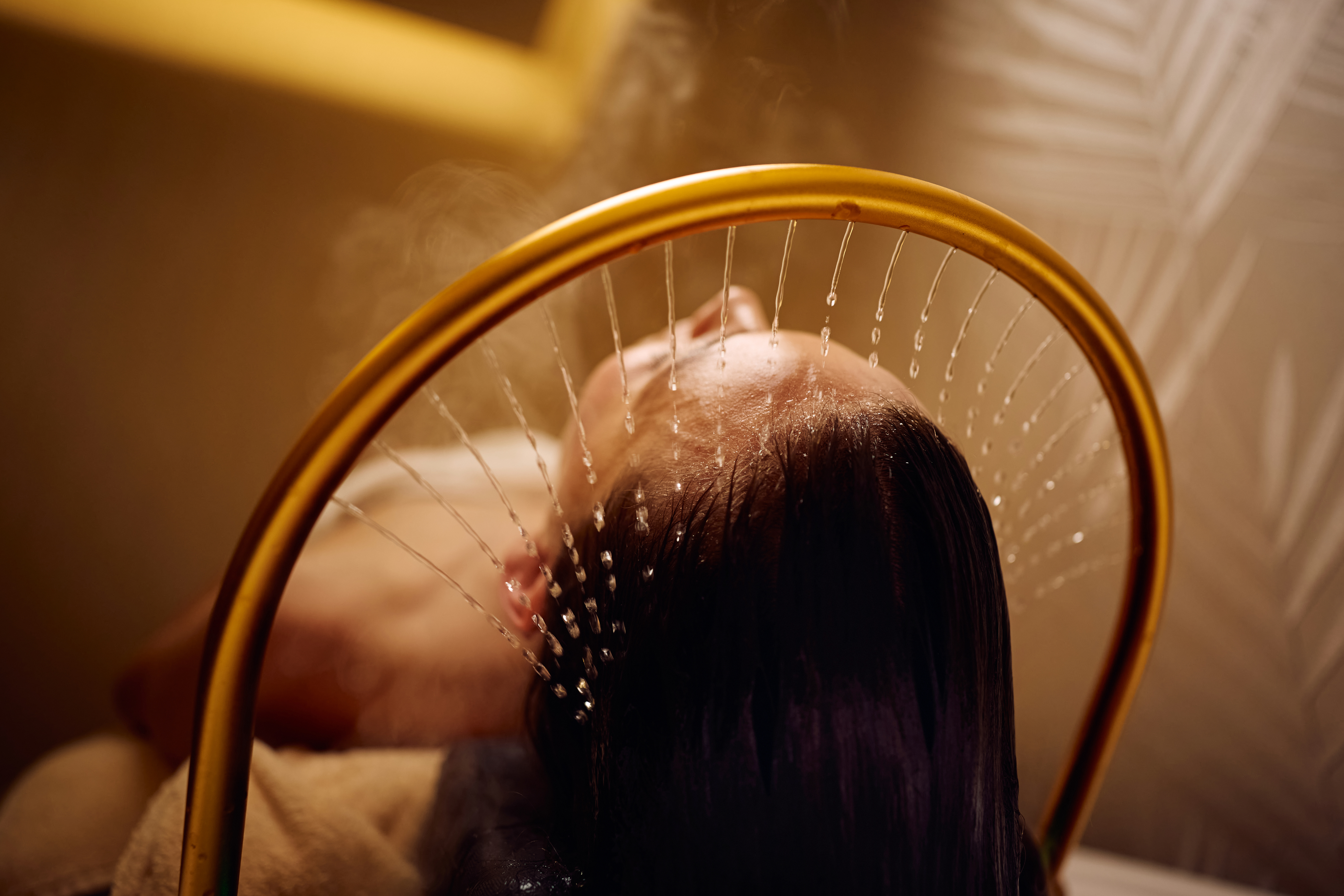 Person rinsing hair under a golden showerhead with water streaming down