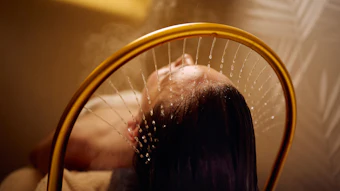 Person rinsing hair under a golden showerhead with water streaming down
