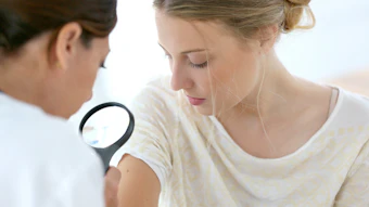 Dermatologist examining patient's skin with magnifying glass during medical consultation