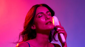 Woman with closed eyes holding a neon light stick against vibrant pink and purple gradient background