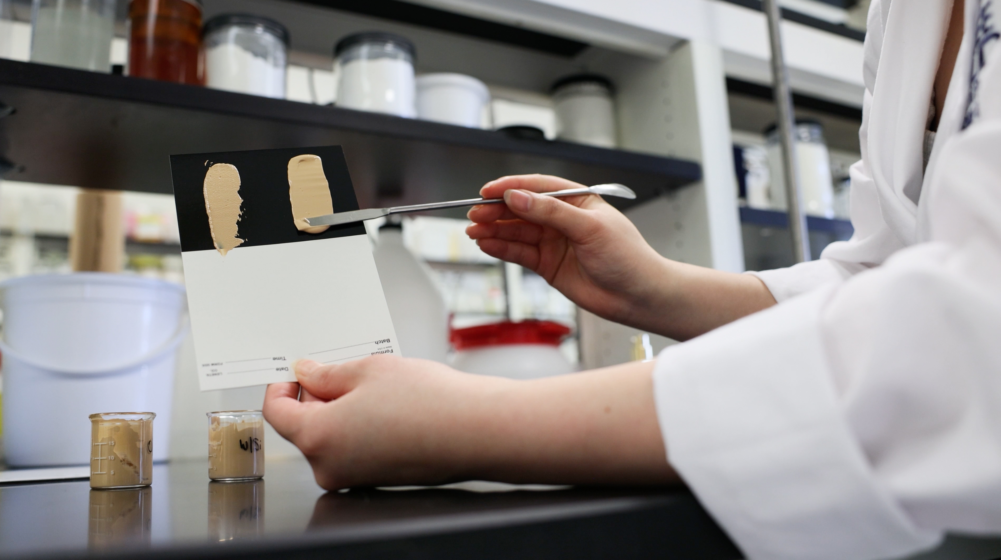 Scientist examining foundation or cosmetic color swatches with brush in laboratory setting