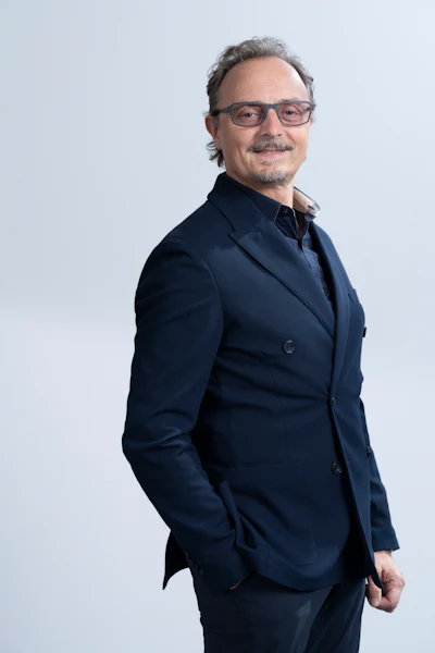 Professional portrait of a man wearing glasses and dark blazer against neutral background