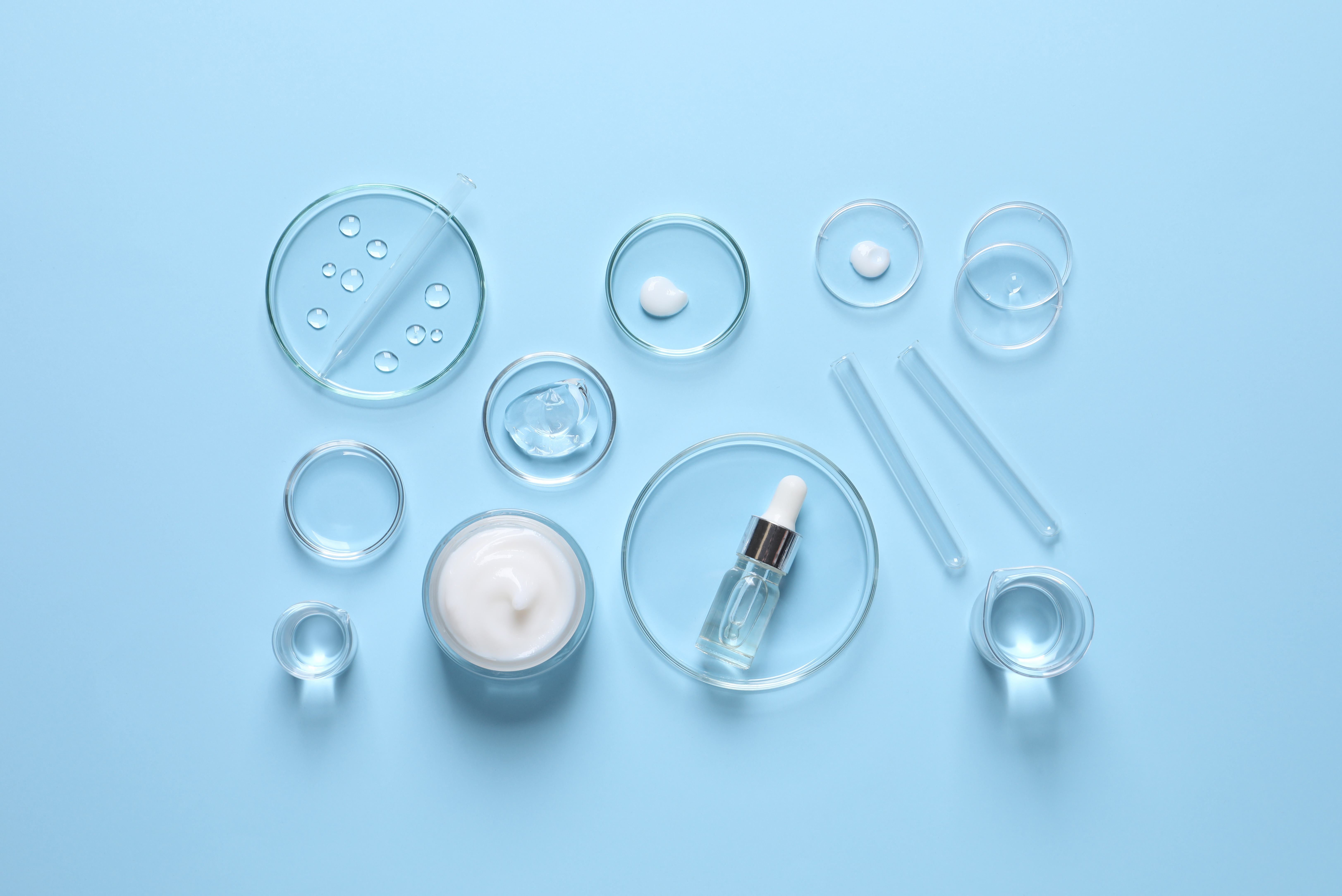 Skincare laboratory setup with glass petri dishes, serums, and cosmetic products on blue background