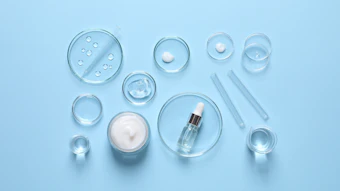 Skincare laboratory setup with glass petri dishes, serums, and cosmetic products on blue background