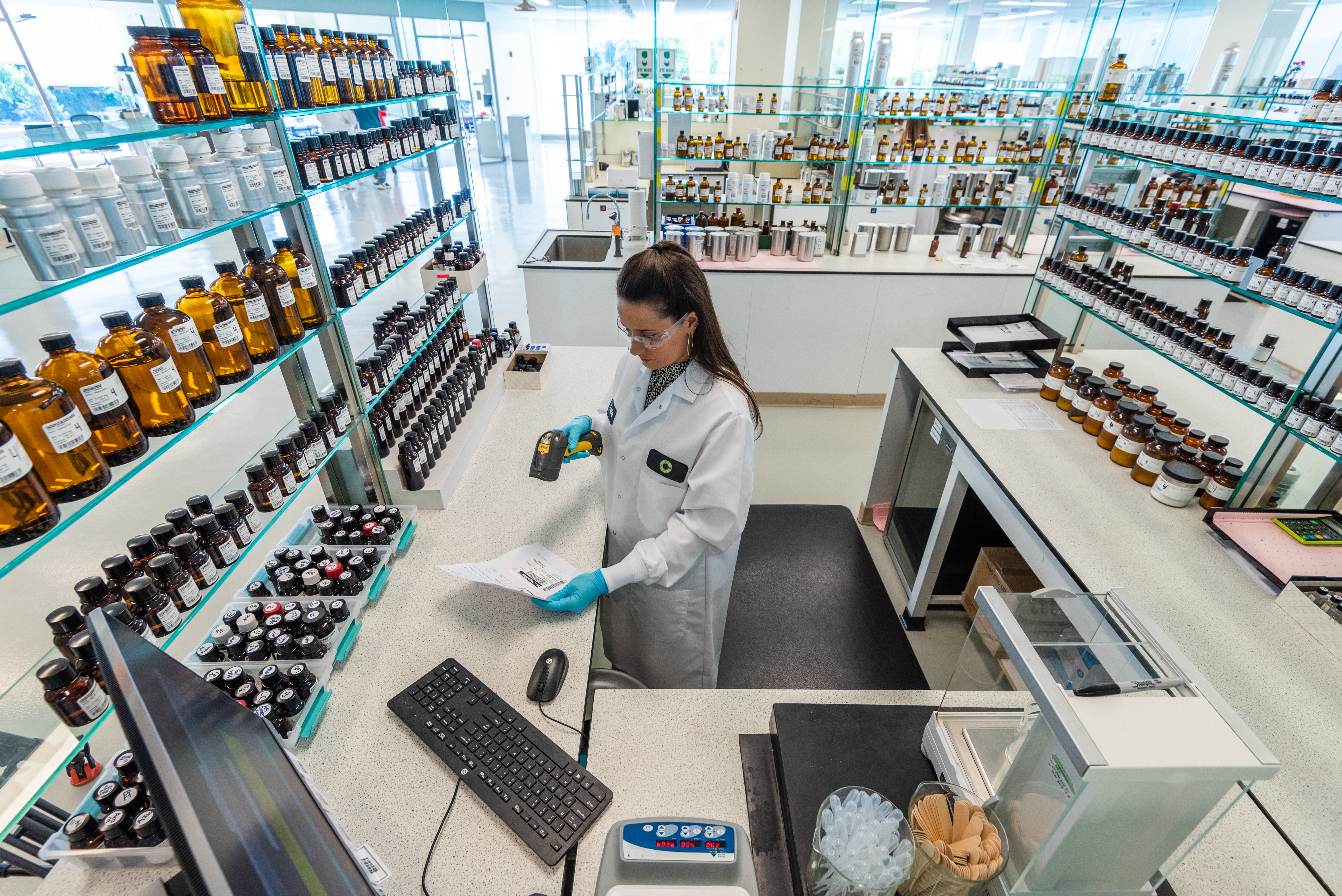 Scientist in lab coat working at bench with shelves of bottles and products in modern laboratory