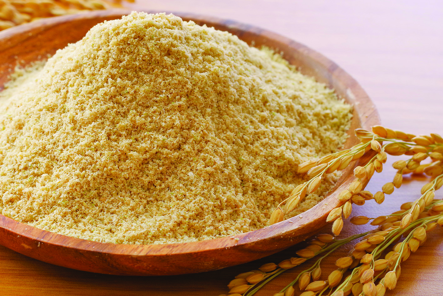 Fine wheat flour in wooden bowl with golden wheat stalks on neutral background