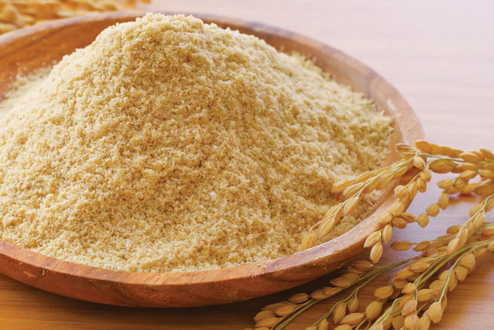 Fine wheat flour in wooden bowl with golden wheat stalks on neutral background