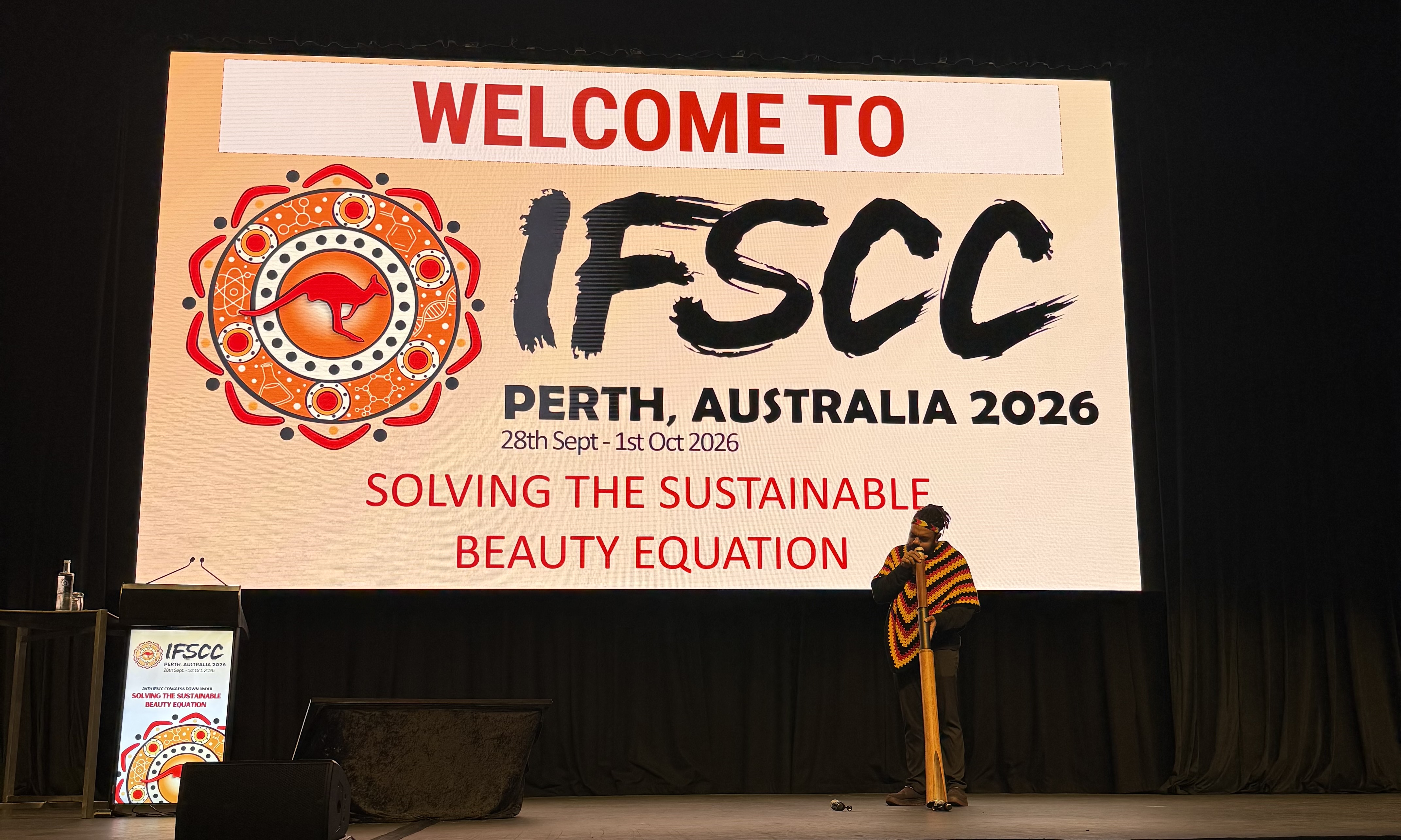IFSCC Perth 2026 conference welcome slide with ornate red logo and speaker on stage