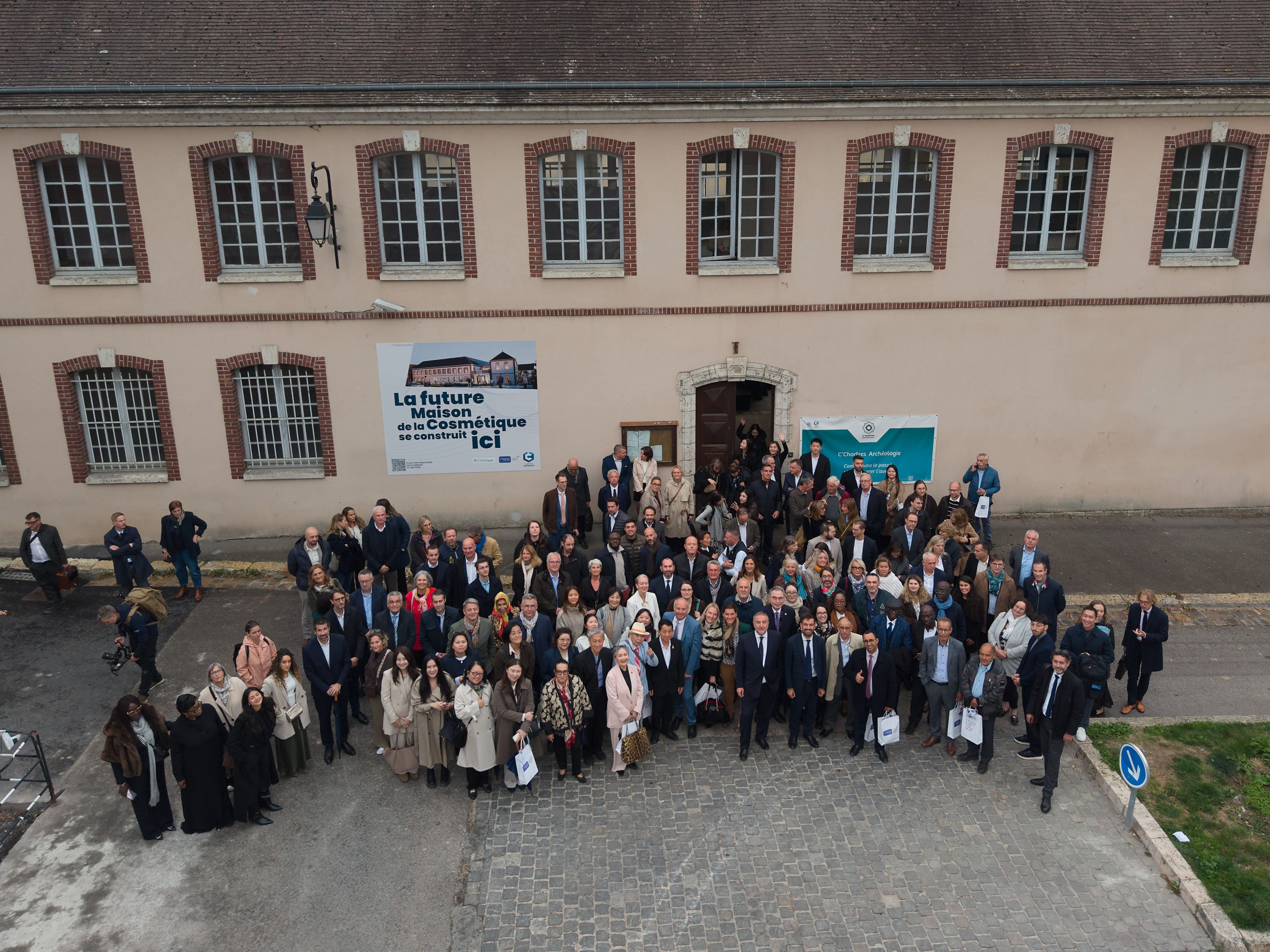 Large group of formally dressed professionals gathered outside historic brick building for official event or conference