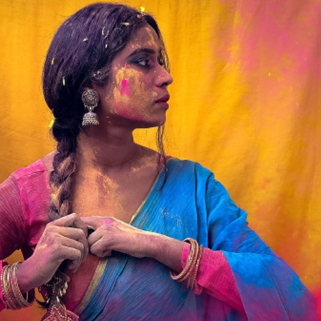 Woman in blue and pink traditional attire with colorful face paint and braided hair against warm gradient background