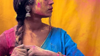 Woman in blue and pink traditional attire with colorful face paint and braided hair against warm gradient background
