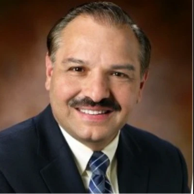 Professional headshot of a smiling middle-aged man in dark suit and blue striped tie